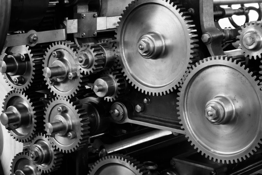 gears-cogs-machine-machinery-159298 Close-up view of a complex industrial gear mechanism in black and white.